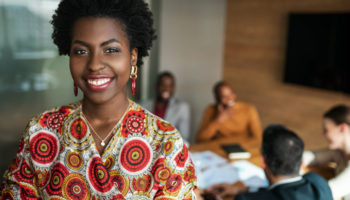 close up of beautiful young smiling professional black african business woman, coworkers hold a meeting in background